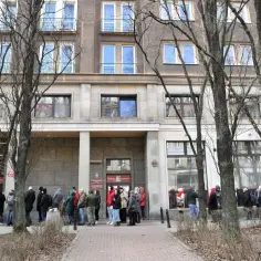 Kolejka przed budynkiem, gdzie wyrabia się paszport. Ludzie stoją na chodniku, czekając na wejście.