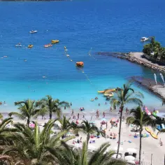 Słoneczne plaże Gran Canarii tętnią życiem. Ludzie kąpią się w turkusowej wodzie, opalają na piasku i korzystają z wodnych atrakcji.