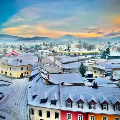 Zimowy krajobraz małego miasteczka w Czechach, idealny na weekend blisko granicy. Dachy pokryte śniegiem, góry w oddali.