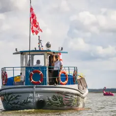 Statek "Mila Mielno" płynie po Jeziorze Jamno. Na pokładzie widać dwóch mężczyzn, jeden z nich pali papierosa.