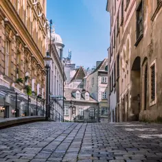 Urokliwa, brukowana uliczka w Wiedniu, gdzie historyczna architektura i niebo tworzą malowniczy widok. Ceny w Wiedniu mogą być różne, ale piękno miasta jest bezcenne.
