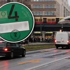 Wjazd do Berlina samochodem. Zielona naklejka Umweltzone z numerem 4 na szybie auta. W tle pociąg i budynki.
