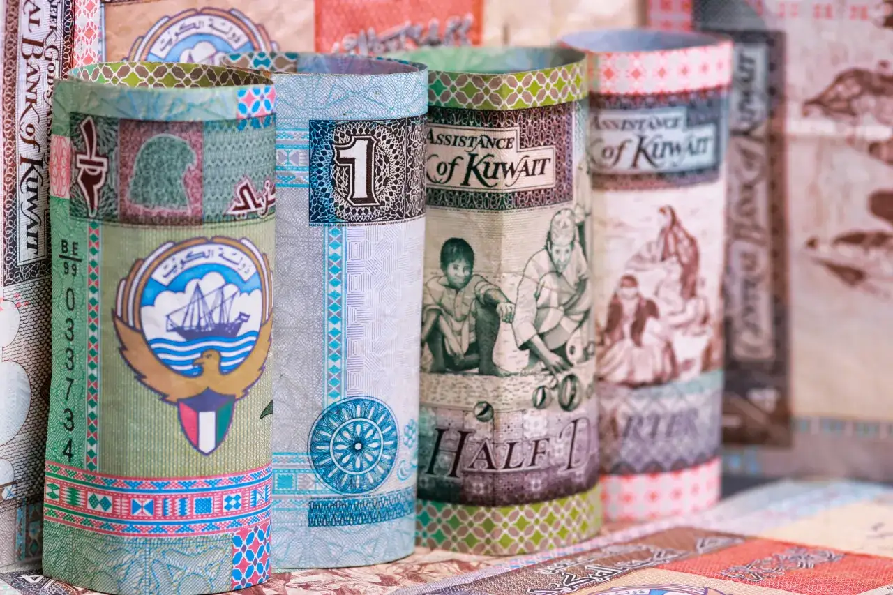Zrolowane banknoty z Kuwejtu, gdzie znajduje się jaka jest najtańsza waluta na świecie. Widoczne są godło, żaglowiec i ludzie.
