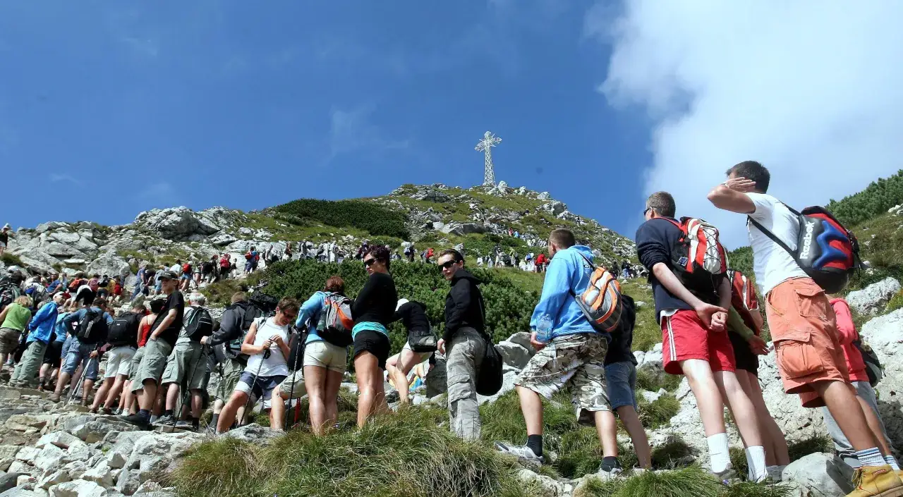 Tłum turystów wspina się na Giewont. Widać krzyż na szczycie.