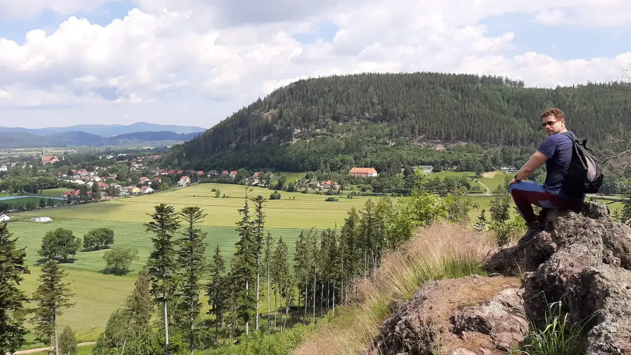 Widok na polskie miasta przy granicy z Czechami, z turystą siedzącym na skale.