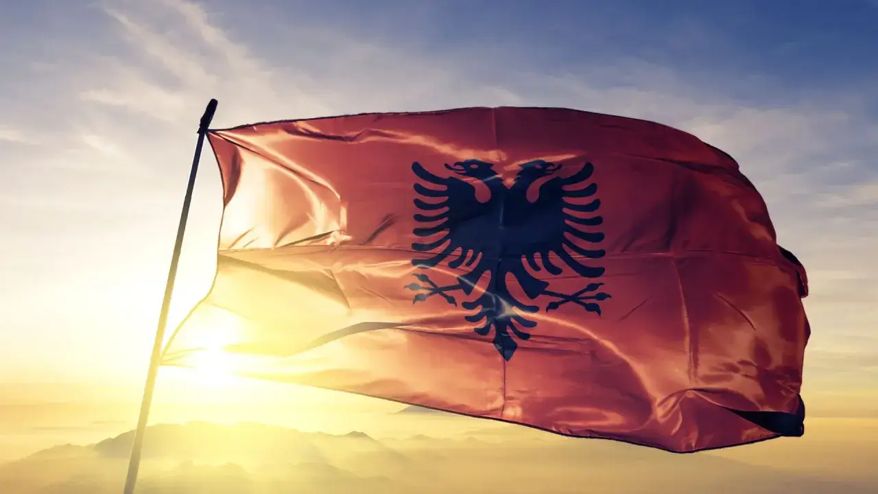 Flaga Albanii powiewa na tle zachodzącego słońca. Czy Albania jest w Unii Europejskiej? To pytanie nurtuje wielu podróżników.