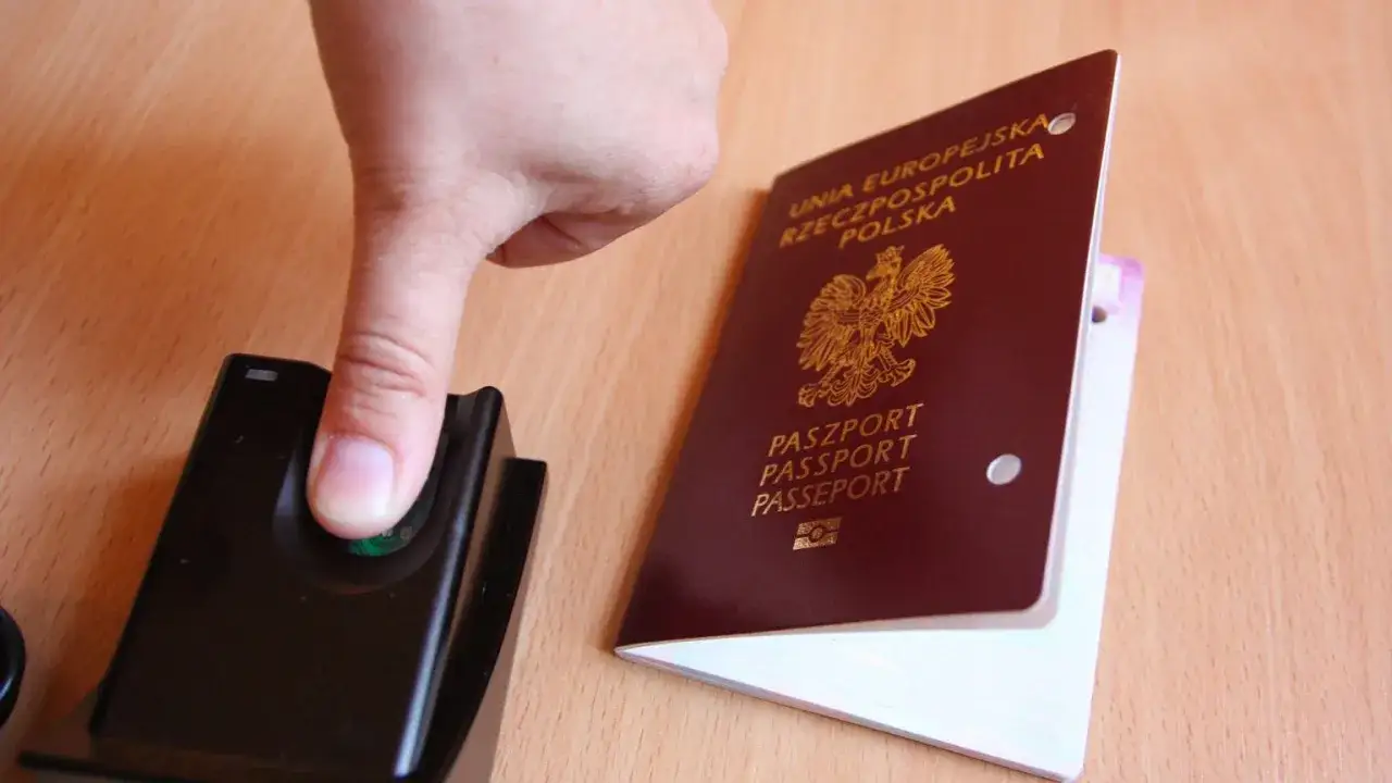 Palec na czytniku obok polskiego paszportu. Ważność paszportu dla dorosłego jest kluczowa do podróży.