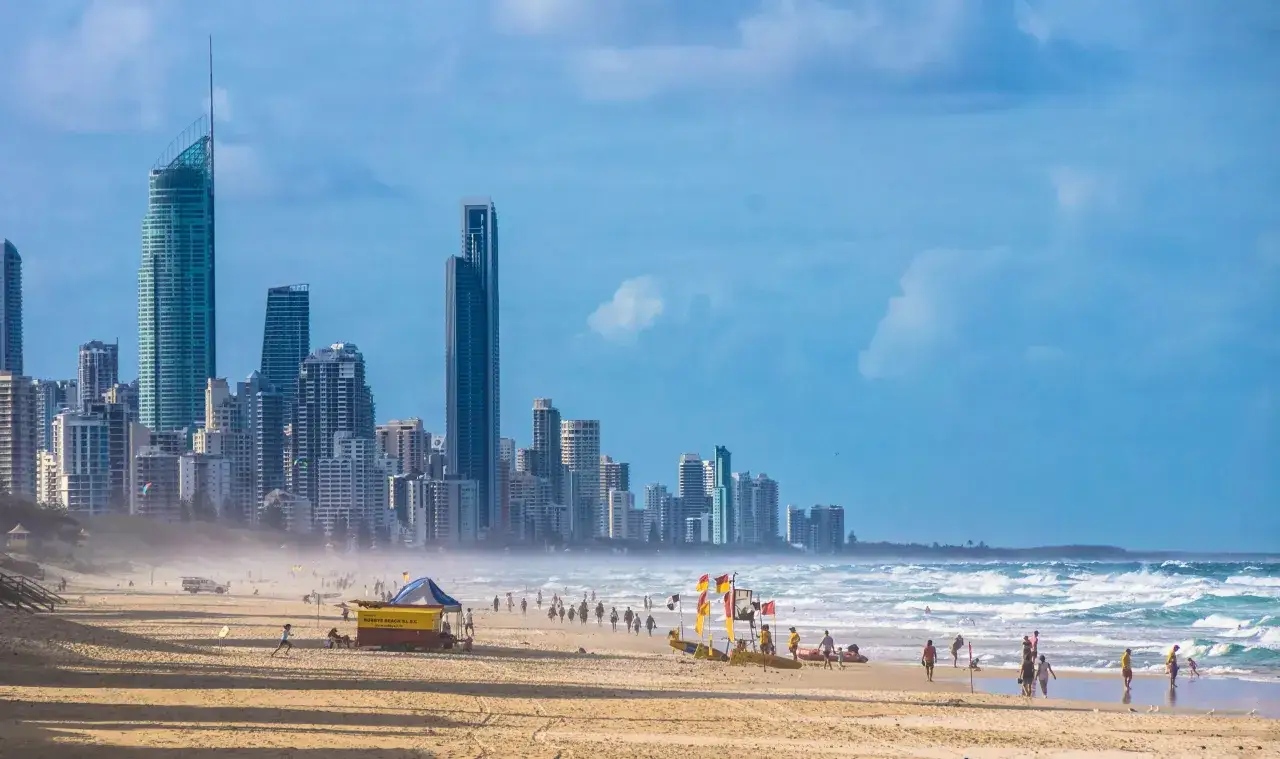 Plaża w Australii, z widokiem na drapacze chmur i ocean. Ludzie spacerują po piasku, a ratownicy czuwają nad bezpieczeństwem. Wyspa Mako Australia.
