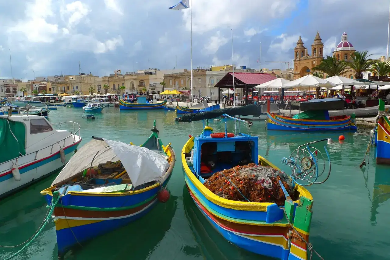 Kolorowe łodzie rybackie w porcie Marsaxlokk. Czy na Malcie jest drogo? Widok sugeruje, że życie toczy się spokojnie, a ceny mogą być przystępne.