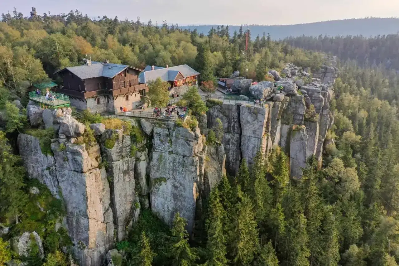 Schronisko na szczycie skalnych wież, blisko granicy z Czechami, otoczone lasem.