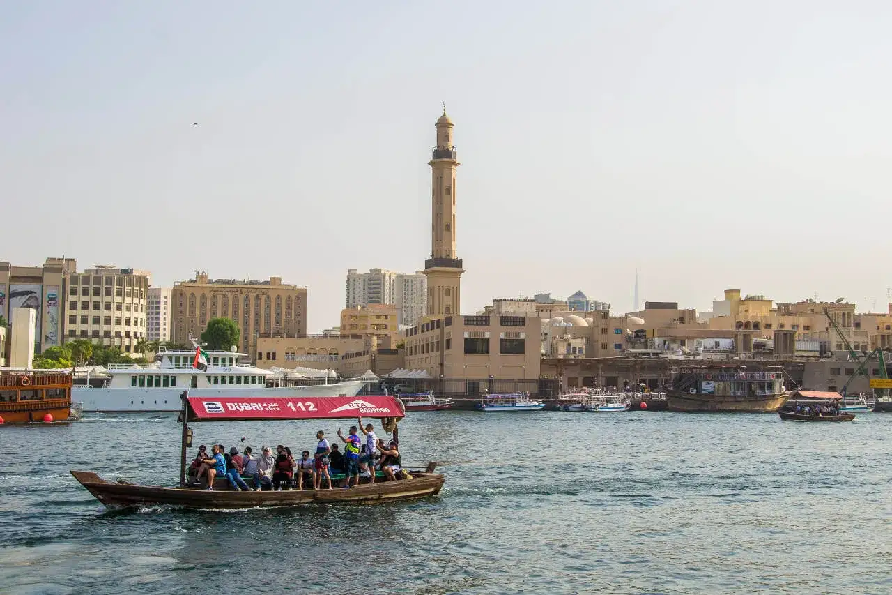 Rejs tradycyjną łodzią po Dubaju. Czy do Dubaju potrzebna jest wiza? Turyści podziwiają panoramę miasta z minaretem.