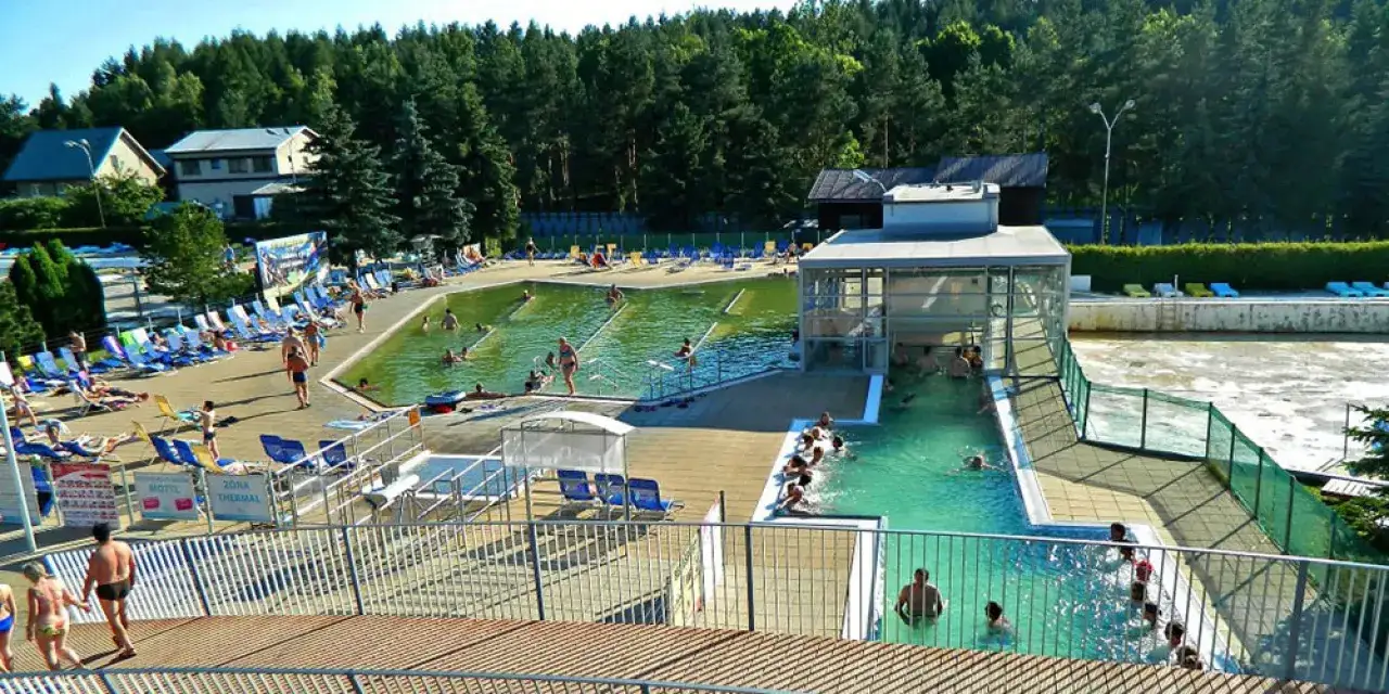 Relaks w termach Czechy blisko granicy. Ludzie kąpią się w basenach, odpoczywają na leżakach wśród zieleni.