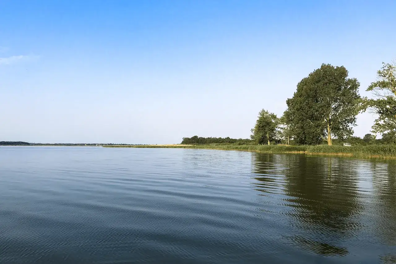 Spokojne wody jeziora Jamno, z widokiem na zielone brzegi i odległe miasto.