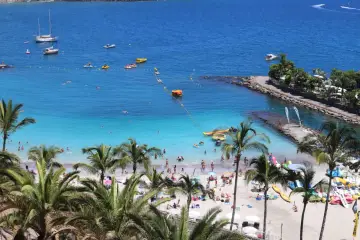 Słoneczne plaże Gran Canarii tętnią życiem. Ludzie kąpią się w turkusowej wodzie, opalają na piasku i korzystają z wodnych atrakcji.