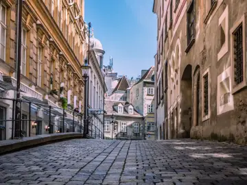 Urokliwa, brukowana uliczka w Wiedniu, gdzie historyczna architektura i niebo tworzą malowniczy widok. Ceny w Wiedniu mogą być różne, ale piękno miasta jest bezcenne.